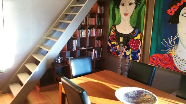 Un coin repas avec une table en bois, des chaises, une bibliothèque et un escalier.