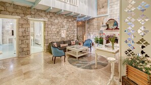 A spacious living area with a stone wall, a high ceiling, and a balcony. - Beyaz Han Hotel (Cesme)