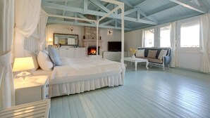 A spacious bedroom with a four-poster bed, a fireplace, a sofa, and a television. - Beyaz Han Hotel (Cesme)