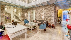 A spacious living area with a stone wall, a staircase, and a balcony. - Beyaz Han Hotel (Cesme)
