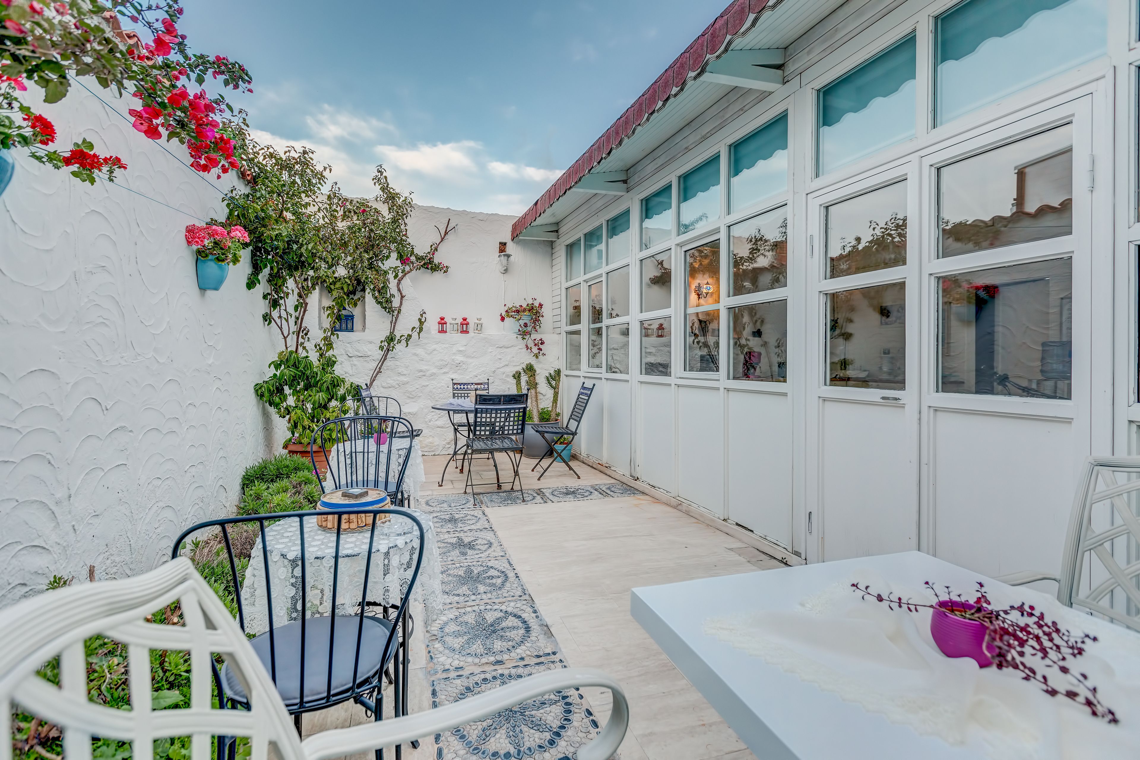 A patio area with white walls, a table, chairs, and potted plants.