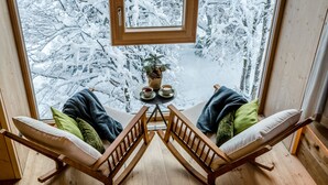A cozy room with a wooden bench and two chairs facing a window. A small table with two cups and a potted plant is visible. - Werdenfelserei (Garmisch-Partenkirchen)