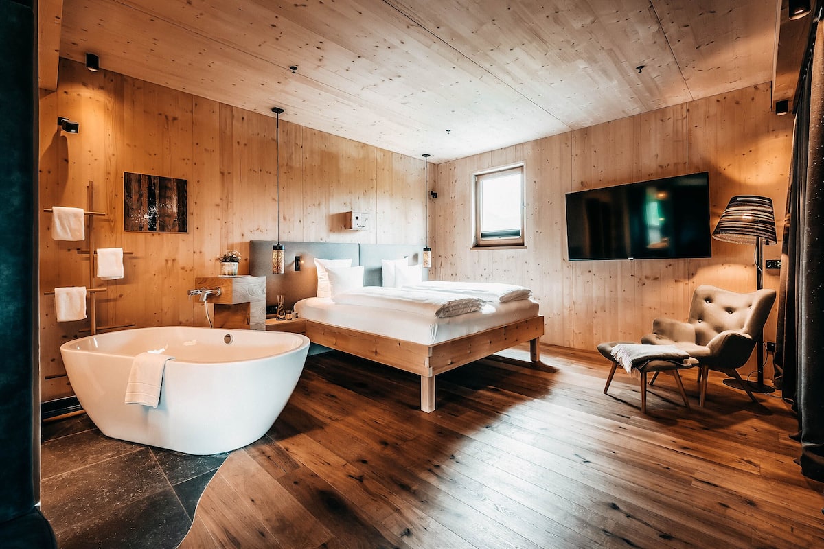Un dormitorio moderno con paredes de madera, una cama grande, una bañera y un televisor.