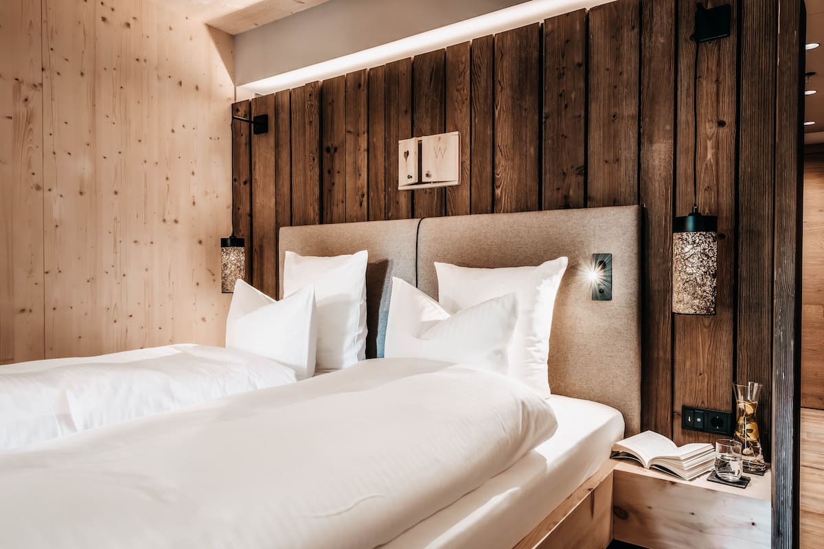 Una cama doble con ropa de cama blanca en una habitación con paredes de madera y un cabecero.