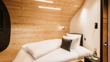 A modern bedroom with a wooden ceiling, a bed with white linens, a dark nightstand, and a vase with flowers.