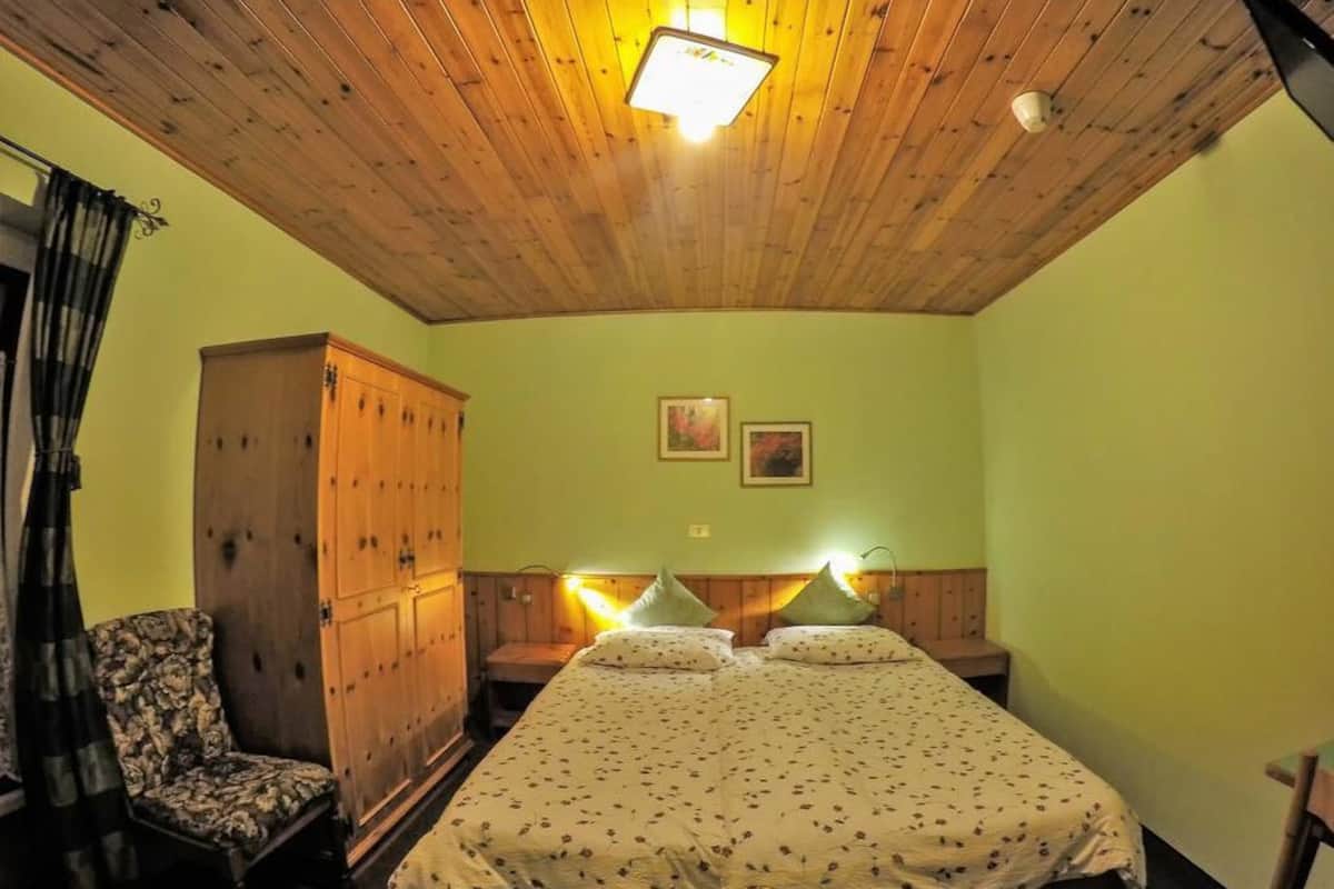 A room with a wooden ceiling, a bed with a floral bedspread, a wooden wardrobe, and a chair.