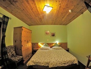 A room with a wooden ceiling, a bed with a floral bedspread, a wooden wardrobe, and a chair. - Cesa Rotic (Canazei)