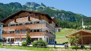 A multi-story wooden building with balconies, set against a mountainous backdrop. - Cesa Rotic (Canazei)