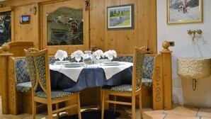 A dining area with wooden paneling, a table set for four, and a bench with floral upholstery. - Cesa Rotic (Canazei)