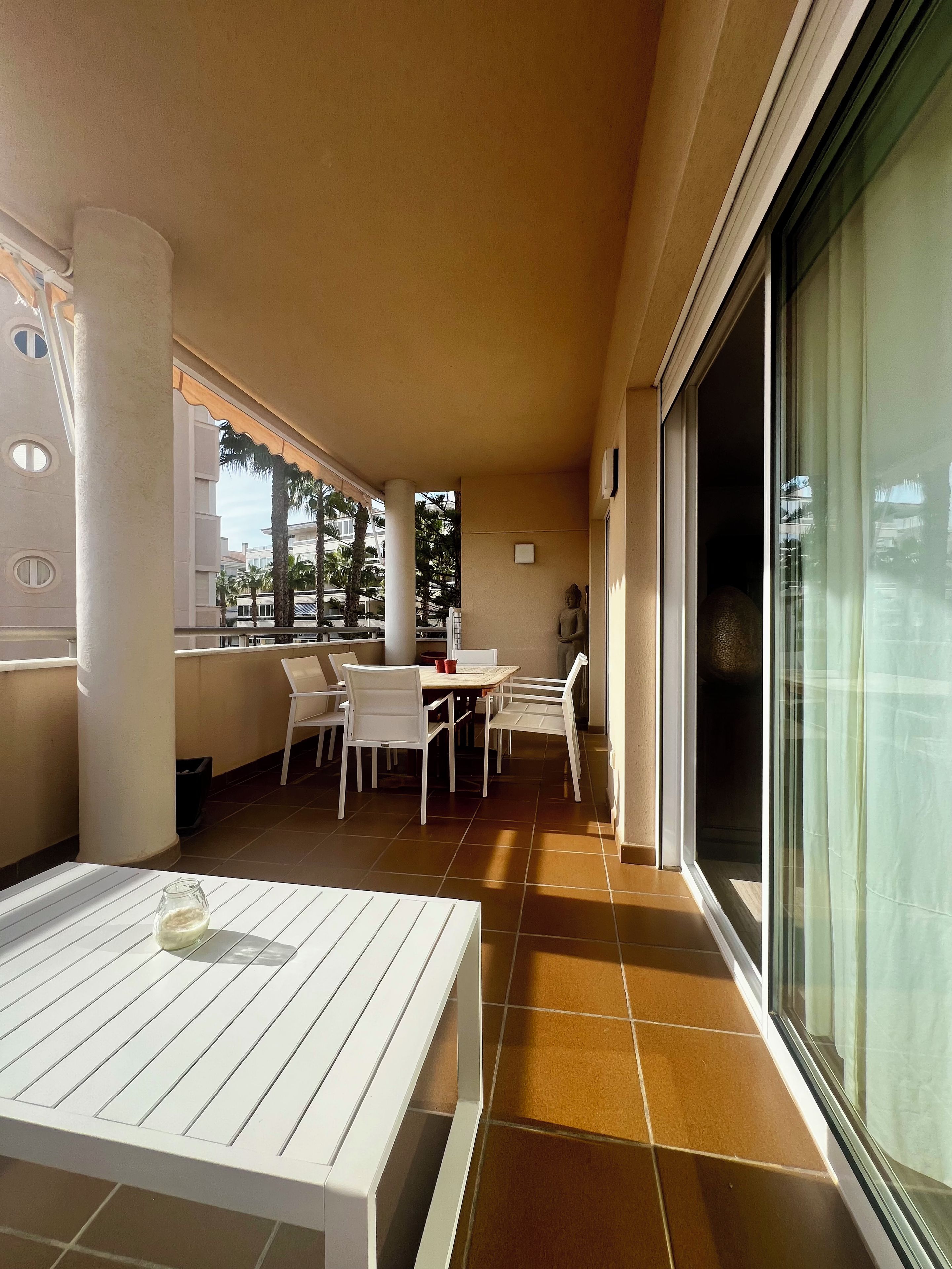 A balcony with a table and chairs, a statue, and a view of palm trees and buildings.