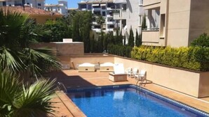 En swimmingpool med solstolar och ett kaklat poolområde, omgiven av grönska och moderna byggnader.