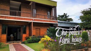 A two-story wooden house with a balcony, a paved entrance, and a sign that reads "The peace Cara house". - The Peace Tara House (Ko Lanta)