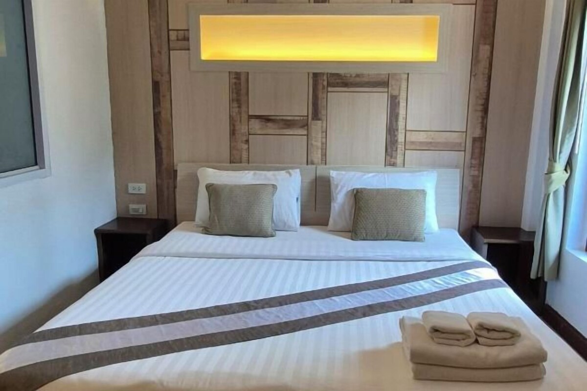 A hotel room with a bed, two nightstands, a headboard with a light panel, and a window with curtains.