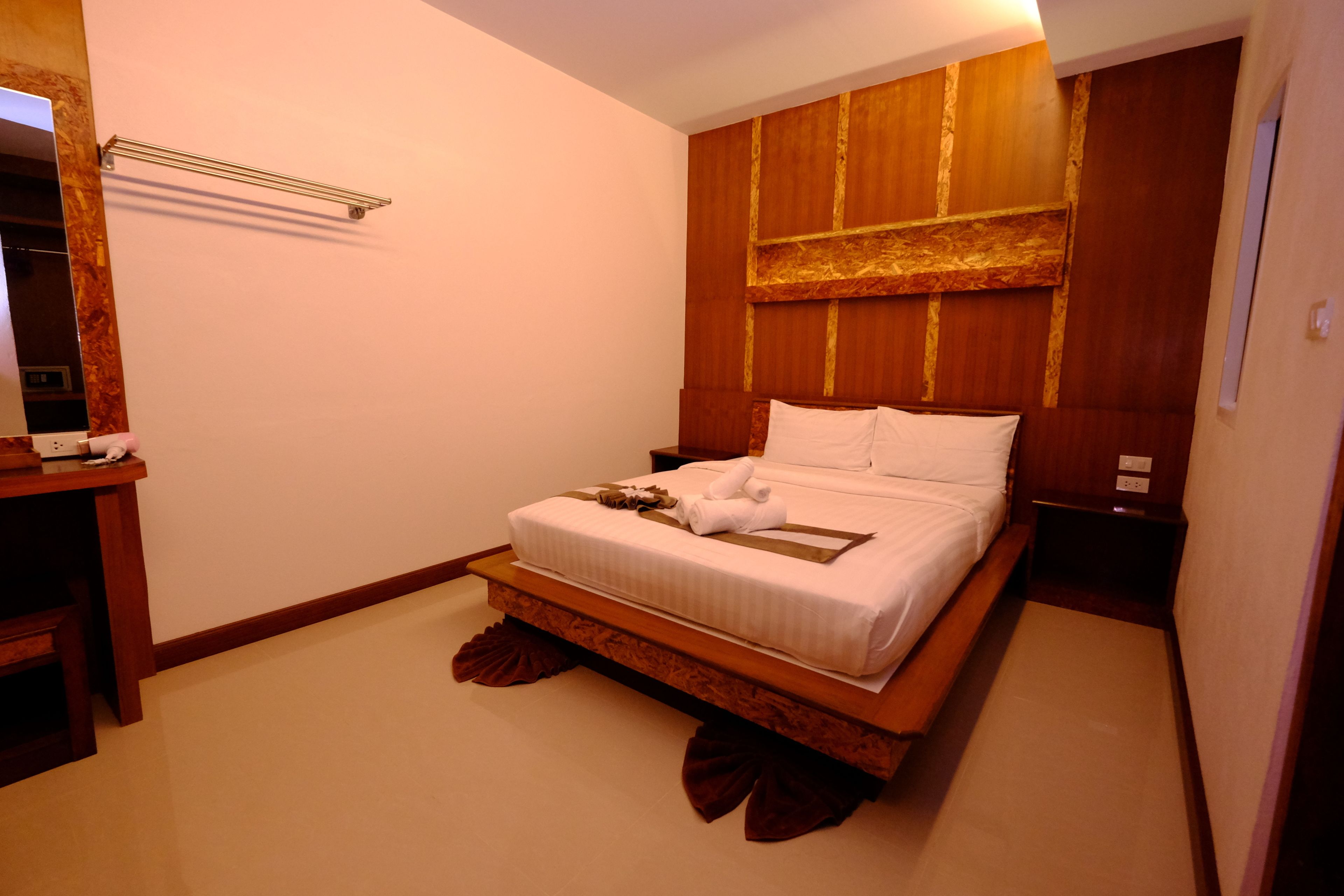 A neatly made bed with white linens and a brown headboard, a bedside table with a lamp, and a wooden shelf above the bed.