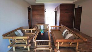 A room with a long wooden sofa set around a central table, wooden walls, and a patterned floor. - The Peace Tara House (Ko Lanta)