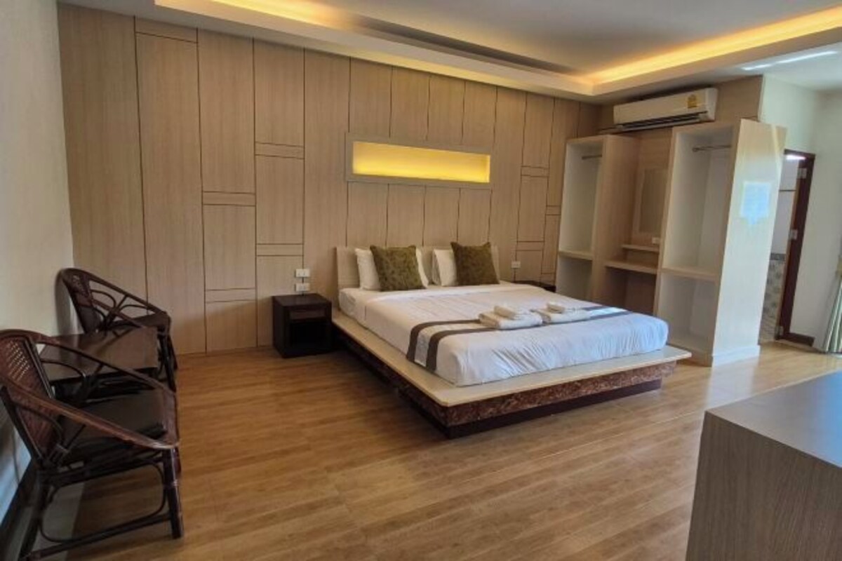 Une chambre d’hôtel moderne avec un grand lit, des murs recouverts de panneaux en bois, une table de chevet, une chaise et des étagères intégrées.