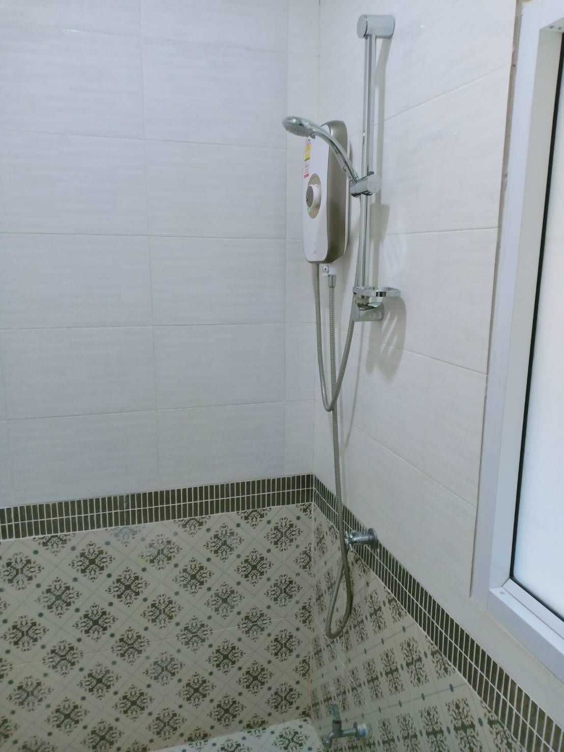 Un baño con ducha, paredes de azulejos y suelo estampado.