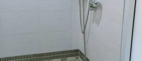 Un baño con ducha, paredes de azulejos y suelo estampado.