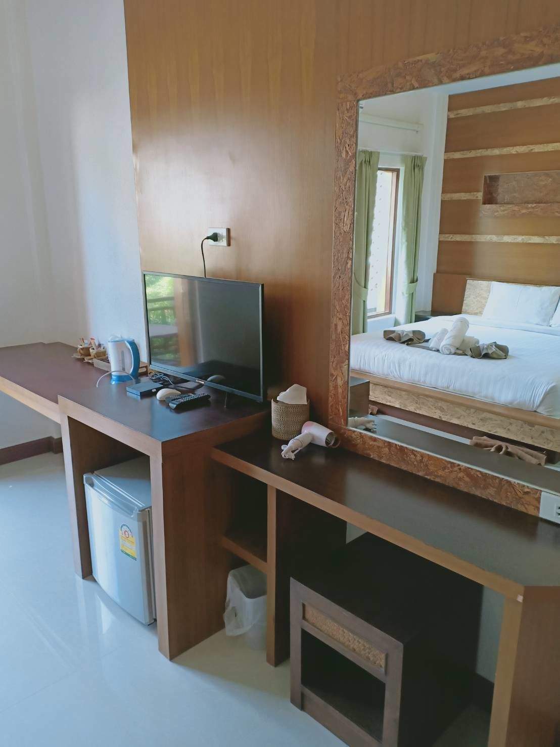 A hotel room with a wooden desk, a television, a bed with neatly made linens, and a small trash bin.