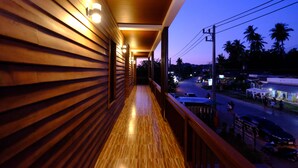 A wooden balcony with a view of a street and palm trees at dusk. - The Peace Tara House (Ko Lanta)