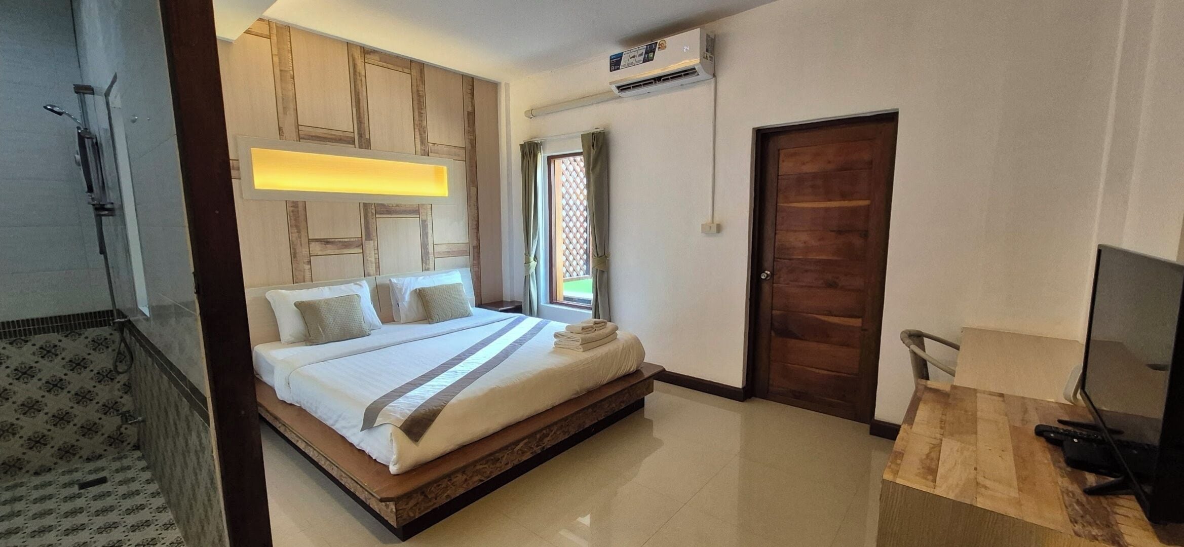 A hotel room with a large bed, a wooden headboard, a TV, and a bathroom with a shower and toilet.