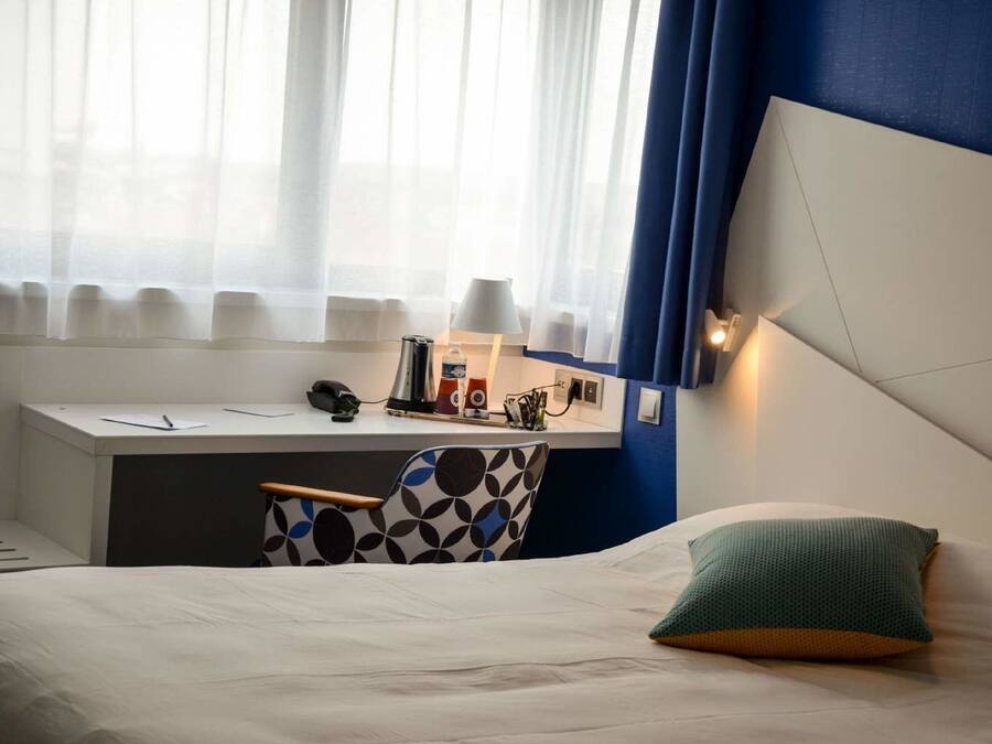 Habitación de hotel con cama, escritorio y silla. Hay una lámpara en el escritorio y un teléfono en la pared.