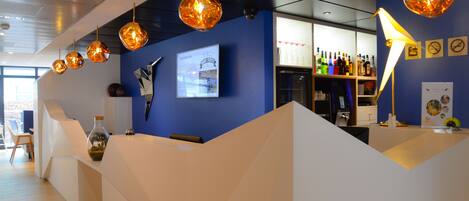A reception area with a blue wall, a bar with various bottles, and hanging spherical light fixtures.