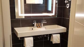 Een moderne badkamer met een wit wastafel, donkere betegelde wanden en een grote spiegel met ingebouwde verlichting.