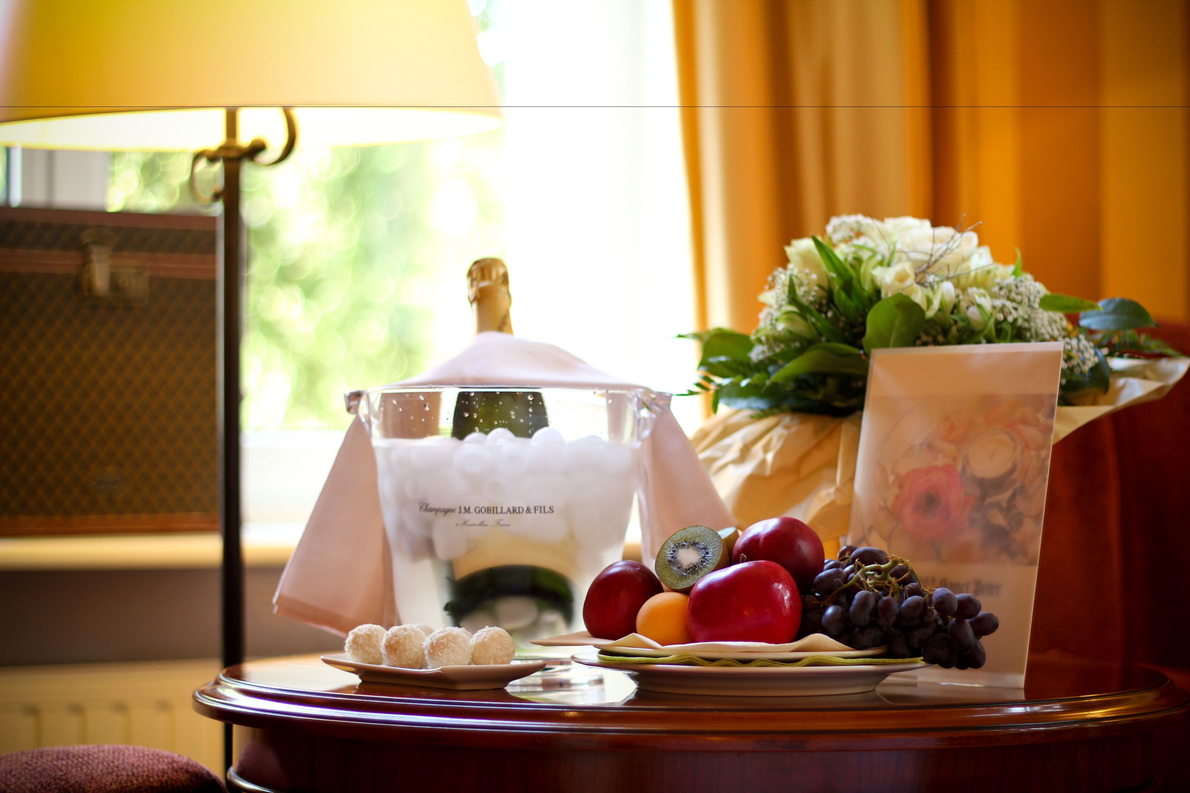 A table with a bottle of champagne, a bouquet of flowers, and a variety of fruits and pastries.