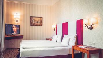 A hotel room with a bed, a television, a painting, and wall sconces.