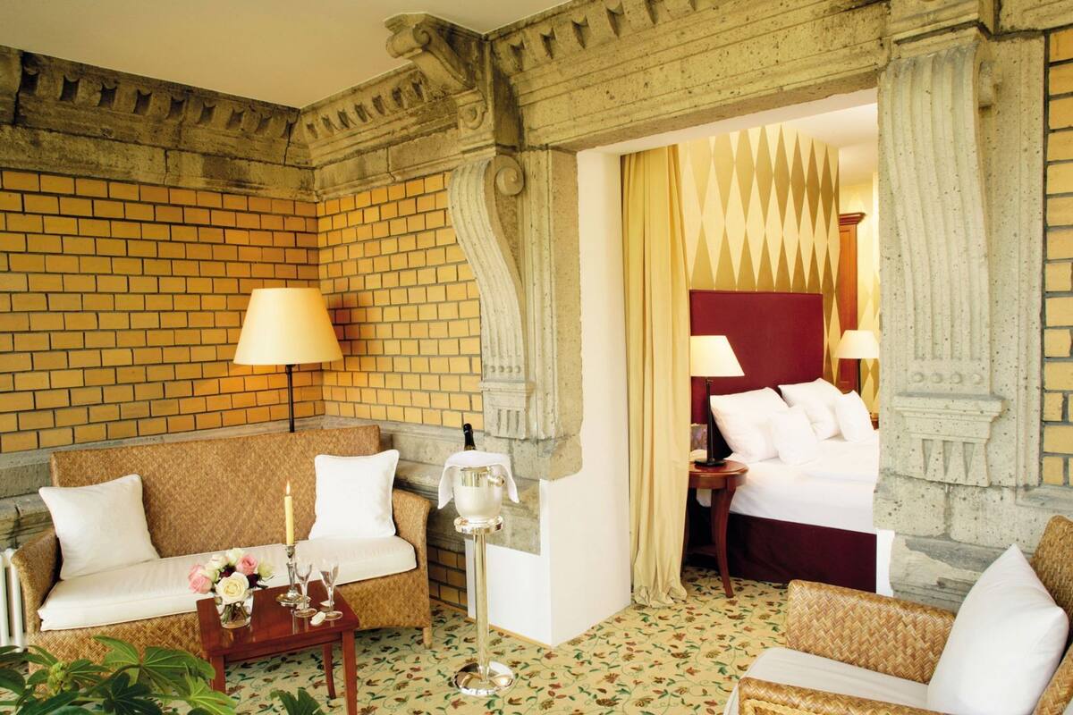 A hotel room with a brick wall, a sofa, a bed, and a table with a bottle and glasses.