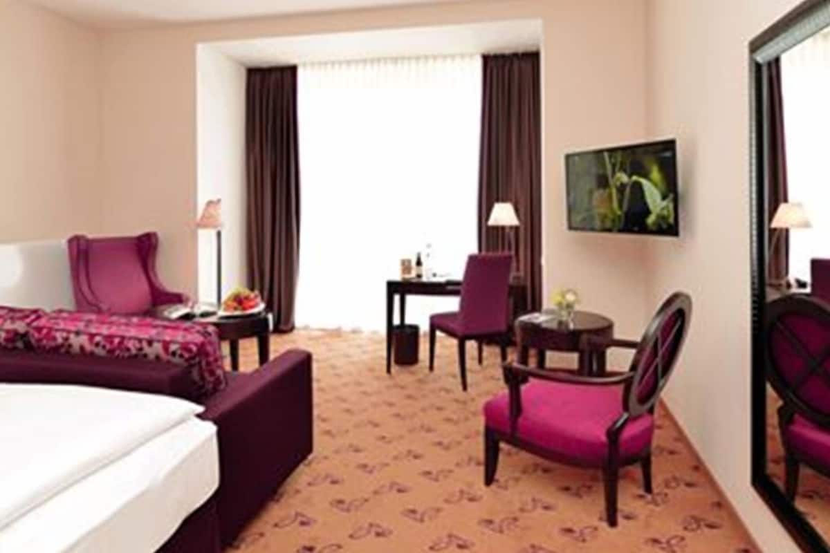 A hotel room with a bed, a desk, a chair, and a small table.