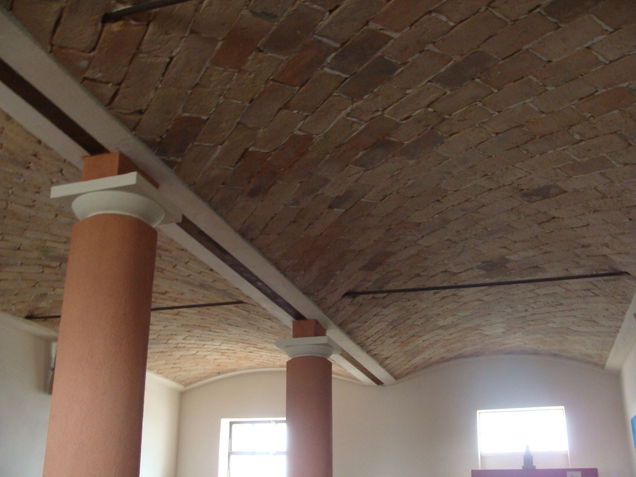 A room with exposed brick ceiling, white walls, and large windows allowing natural light.