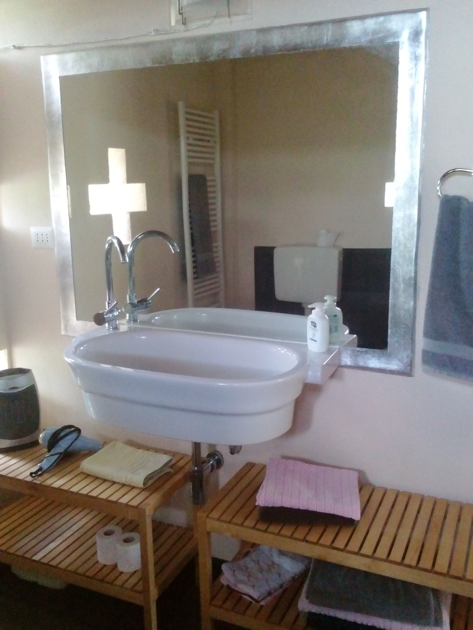 Une salle de bain avec un lavabo blanc, un miroir, un porte-serviettes et une étagère en bois où sont rangés les articles de toilette.