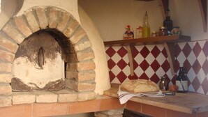 Forno de tijolos com um pão sobre um pano, uma garrafa de azeite e frascos em uma prateleira acima.