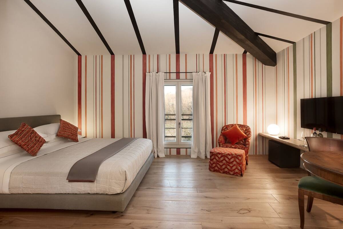 Quarto de hotel com cama, cadeira, televisão e escrivaninha.