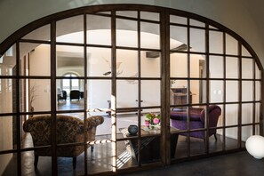 A room with a large arched window, a sofa, a chair, and a table with a vase of flowers.