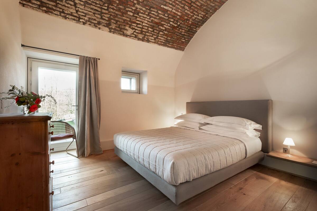 Quarto com cama, cómoda de madeira e janela com cortinas.