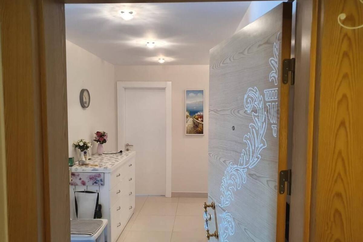 Un pasillo con una puerta blanca, una pequeña mesa con un jarrón de flores, un reloj en la pared y un cuadro enmarcado.