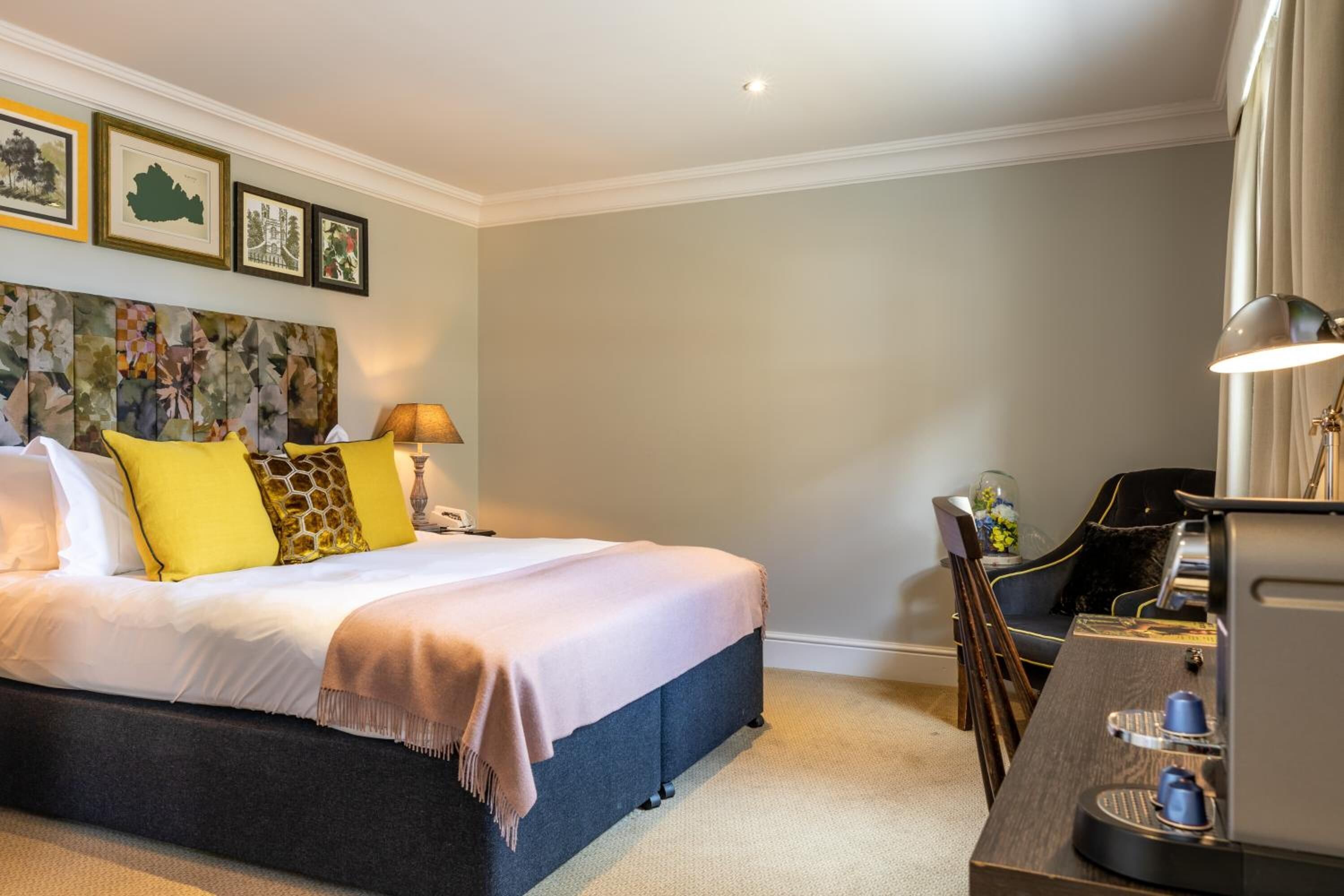 Een hotelkamer met een groot bed, een bureau met een koffiezetapparaat en ingelijste foto's aan de muur.