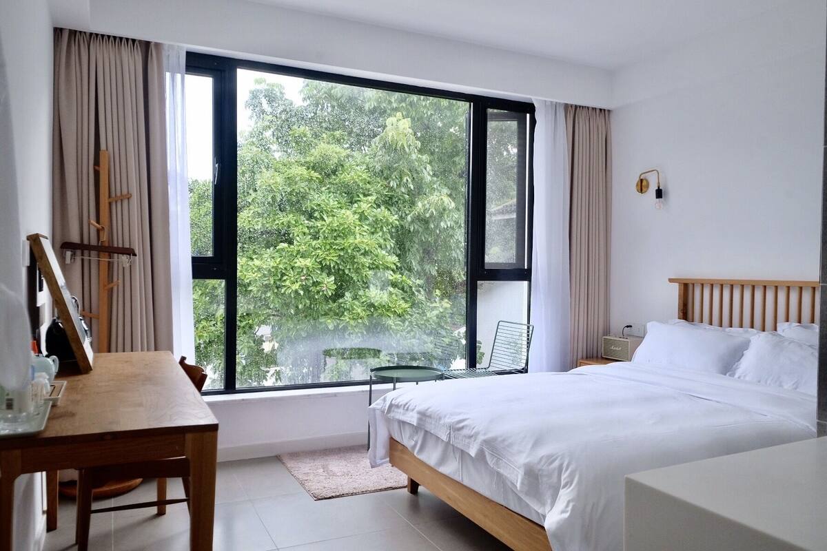 Une chambre d’hôtel avec une grande fenêtre, un lit, un bureau et une chaise.