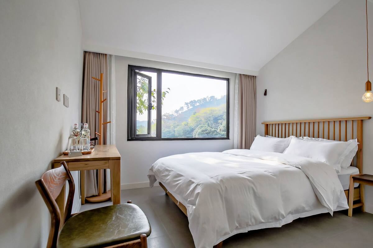 Une chambre avec une grande fenêtre, un lit, un bureau et une chaise.