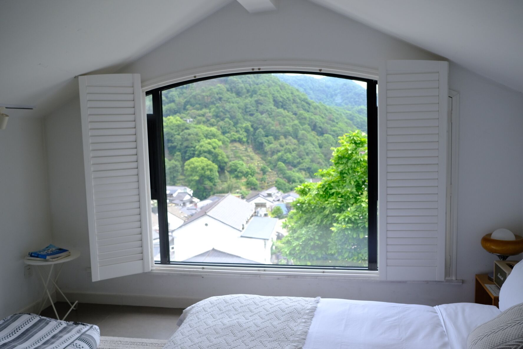 A bedroom with a large window overlooking a forested area.