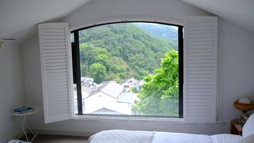 A bedroom with a large window overlooking a forested area.