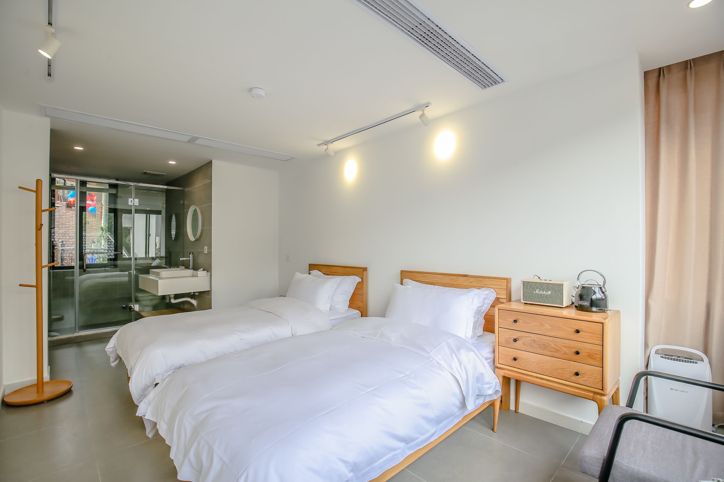 A modern hotel room with two beds, a wooden dresser, a bedside table, and a view of the bathroom.