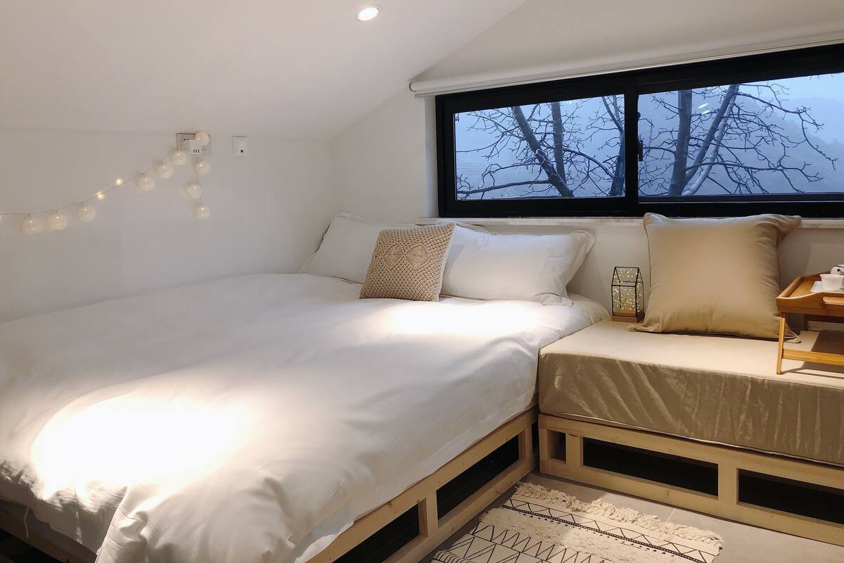 Une chambre à coucher avec un lit, une fenêtre donnant sur des arbres sans feuilles et une table de chevet avec une lampe.