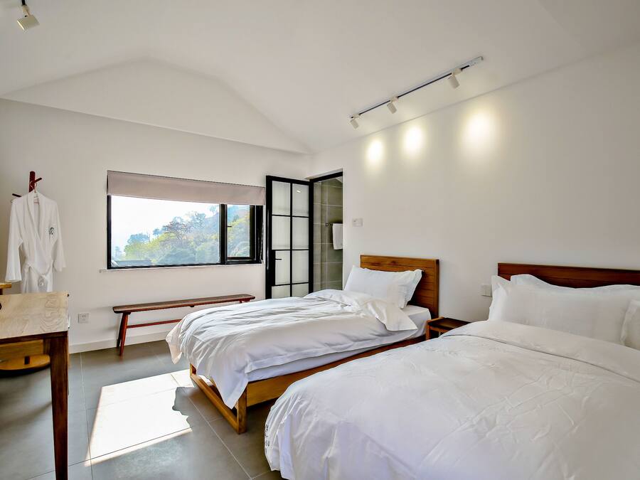 Ein Schlafzimmer mit zwei Betten, einem Holztisch, einer Bank und einem Fenster mit Blick auf Bäume.