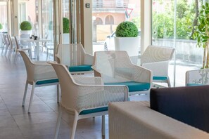 A row of white wicker chairs with teal cushions in a bright, sunlit indoor space with large windows. - Hotel Villa Tirreno (Castagneto Carducci)