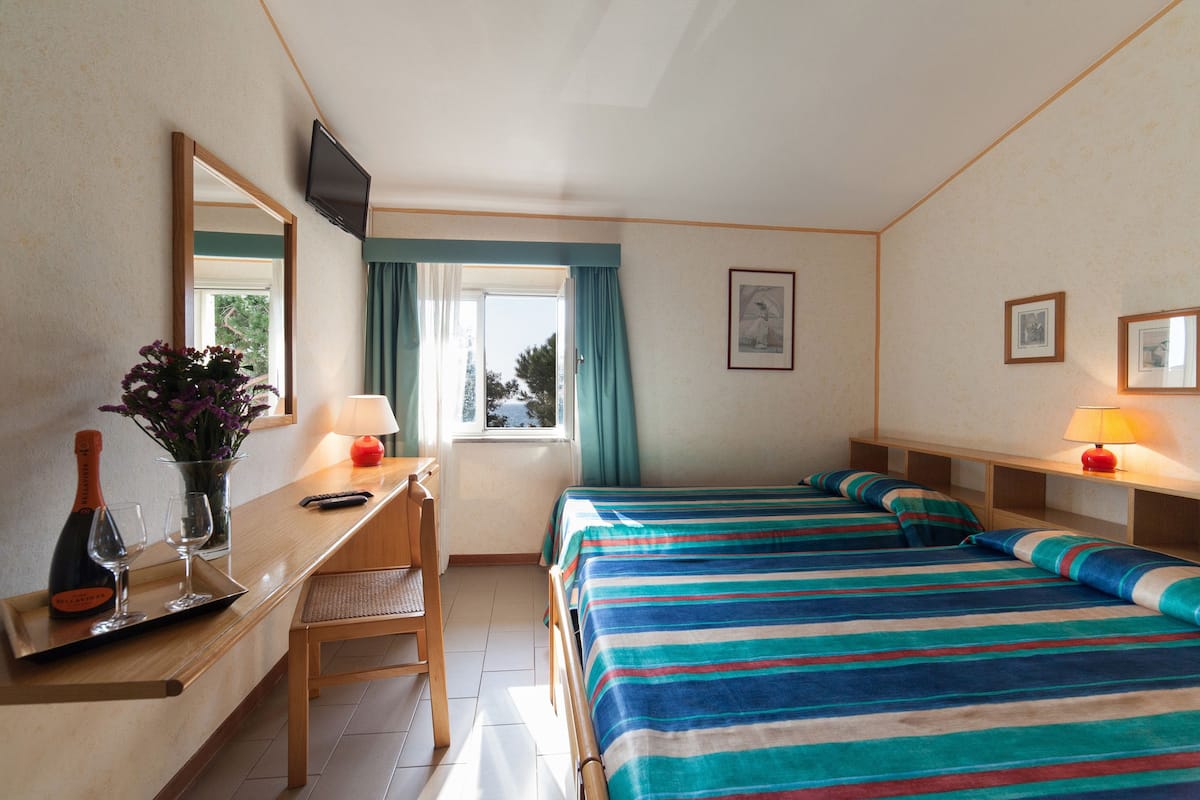 A hotel room with two beds, a desk with a chair, a TV, and a window with curtains.