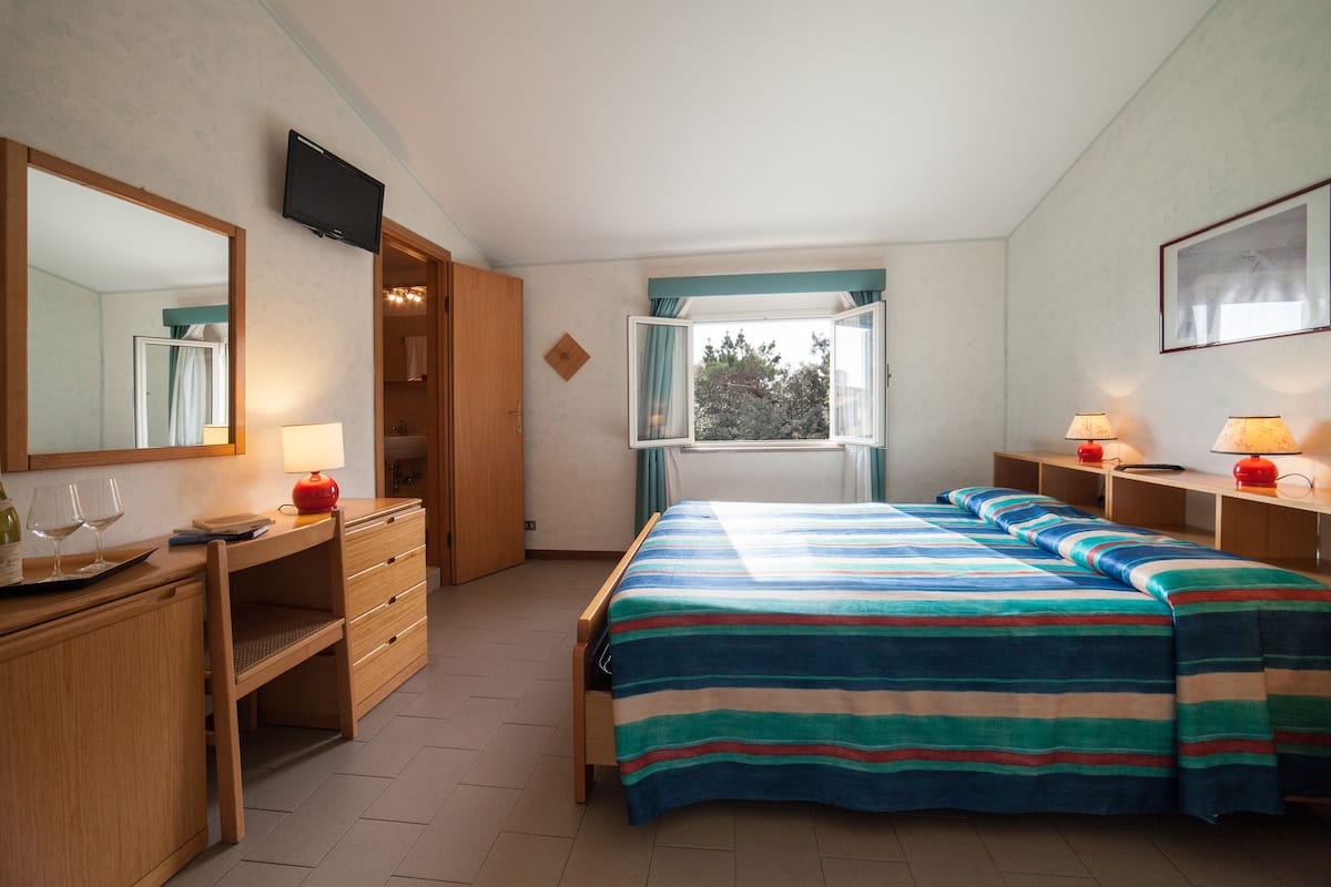 A bedroom with a bed, a desk, a chair, a TV, and a window with curtains.